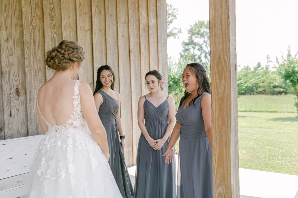 bridesmaids seeing the bride before the outdoor summer wedding at the meadow wedding barn.